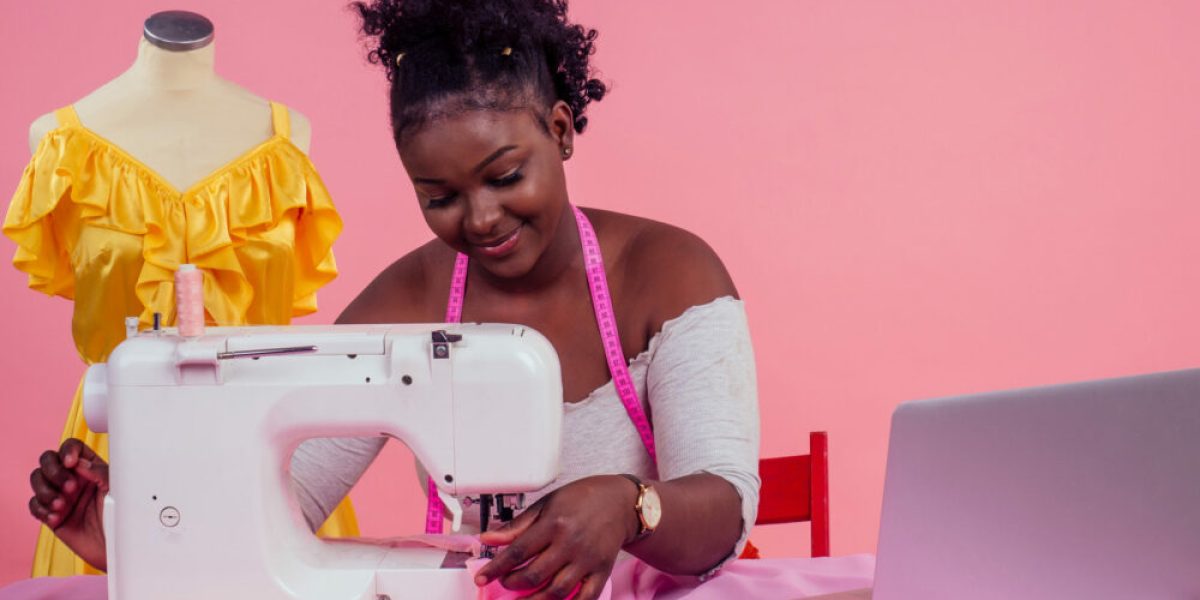 attractive woman seamstress next to the mannequin with sewing machine on pink background in the studio copyspace . concept of idea and inspiration.